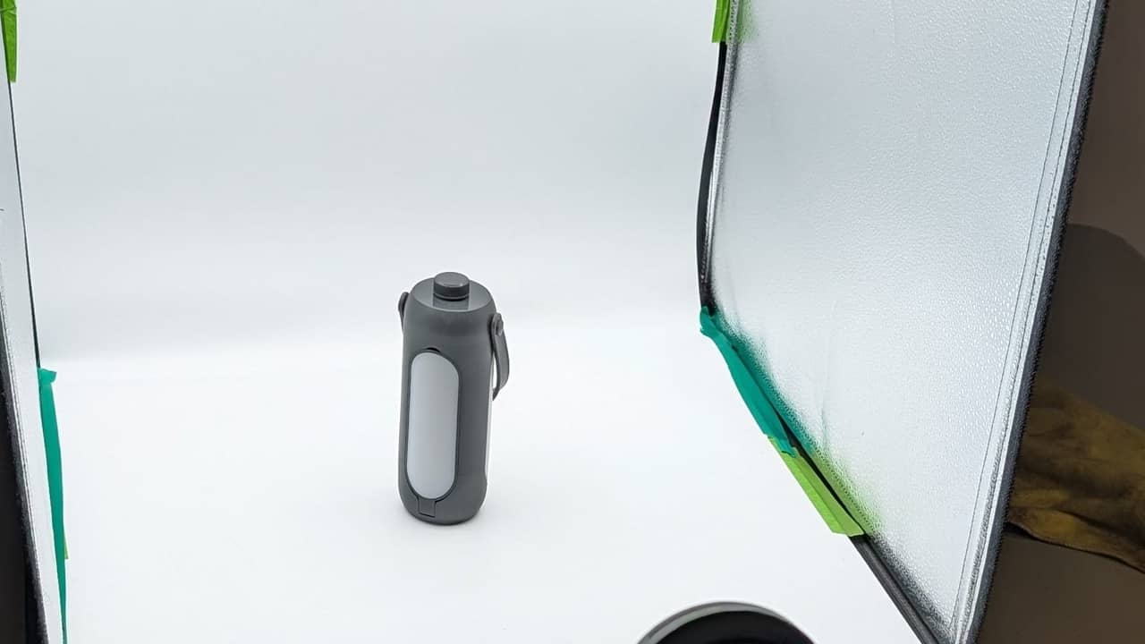 A grey cylindrical product sitting inside a white photography lightbox setup