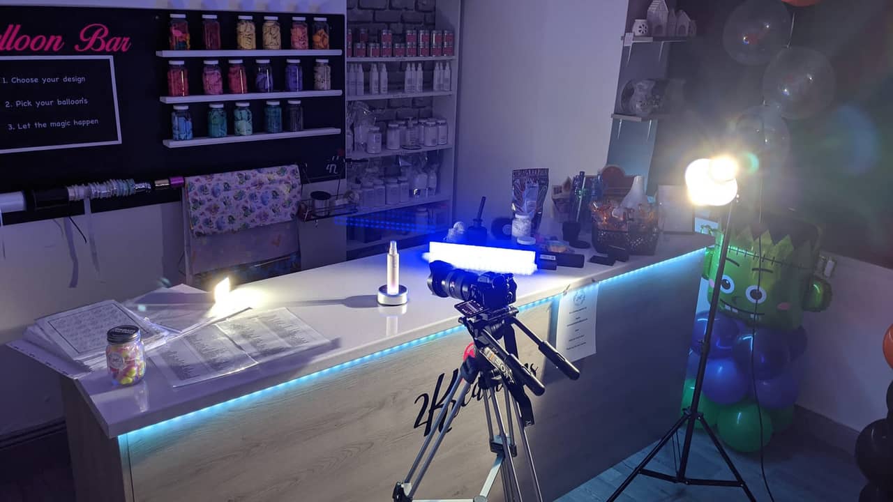 Camera on tripod with ring light and softbox set up at a balloon-shop counter.