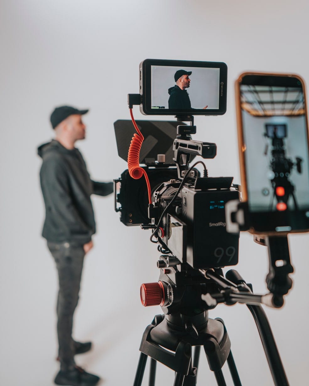 A crew member in the studio beside a cinema camera rig with a field monitor, against a white backdrop
