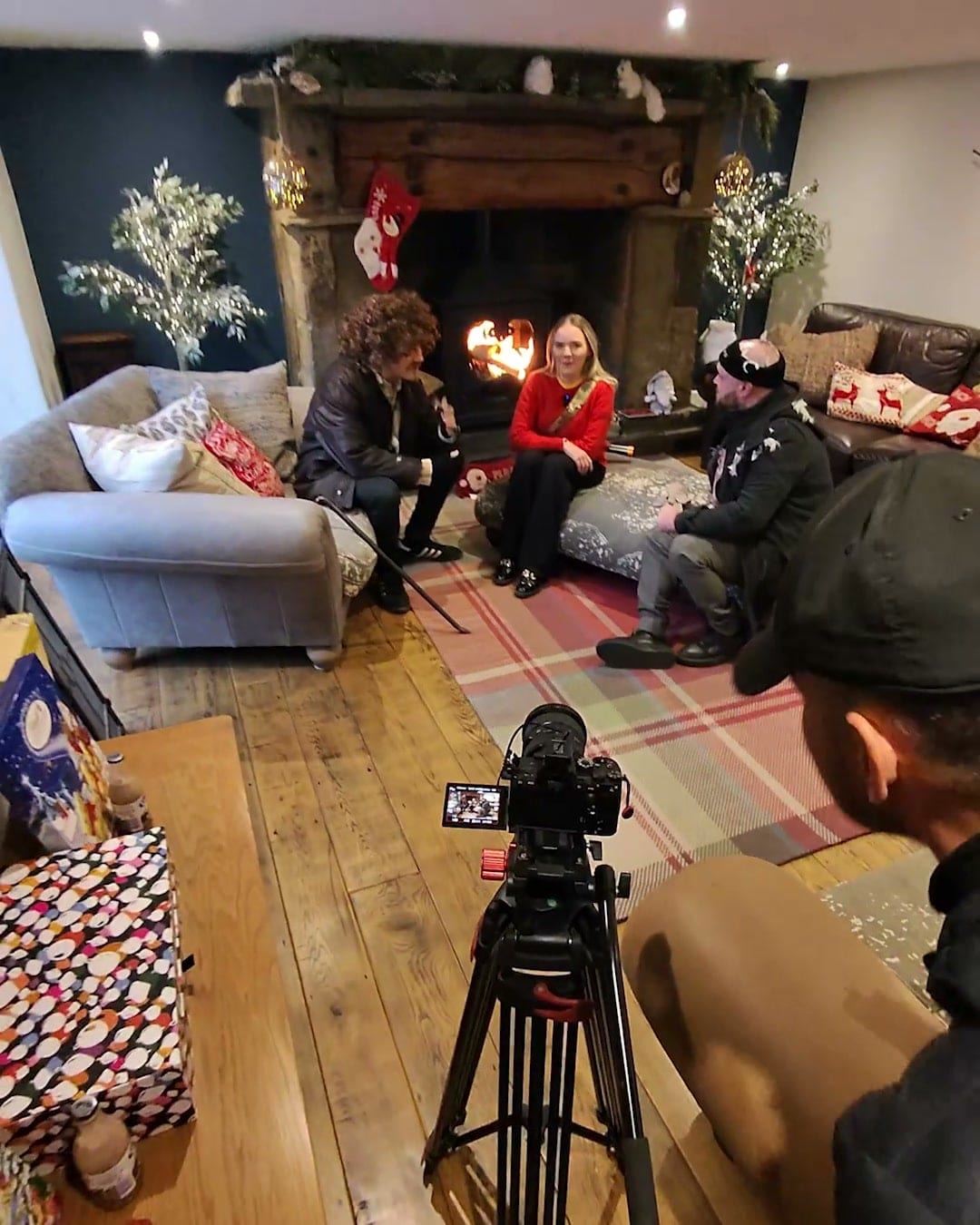 Behind the scenes on a corporate shoot: a camera on a tripod framing a three-person interview by a fireplace