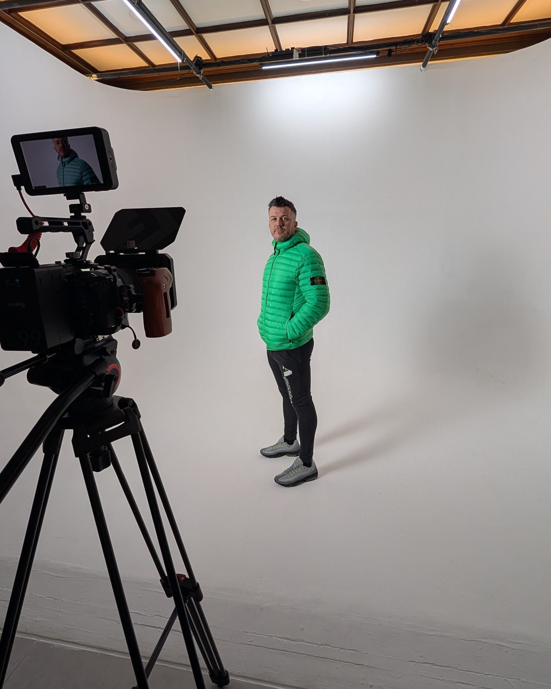 Behind the scenes on a studio shoot: a rigged camera and monitor framing a presenter against the white cyclorama