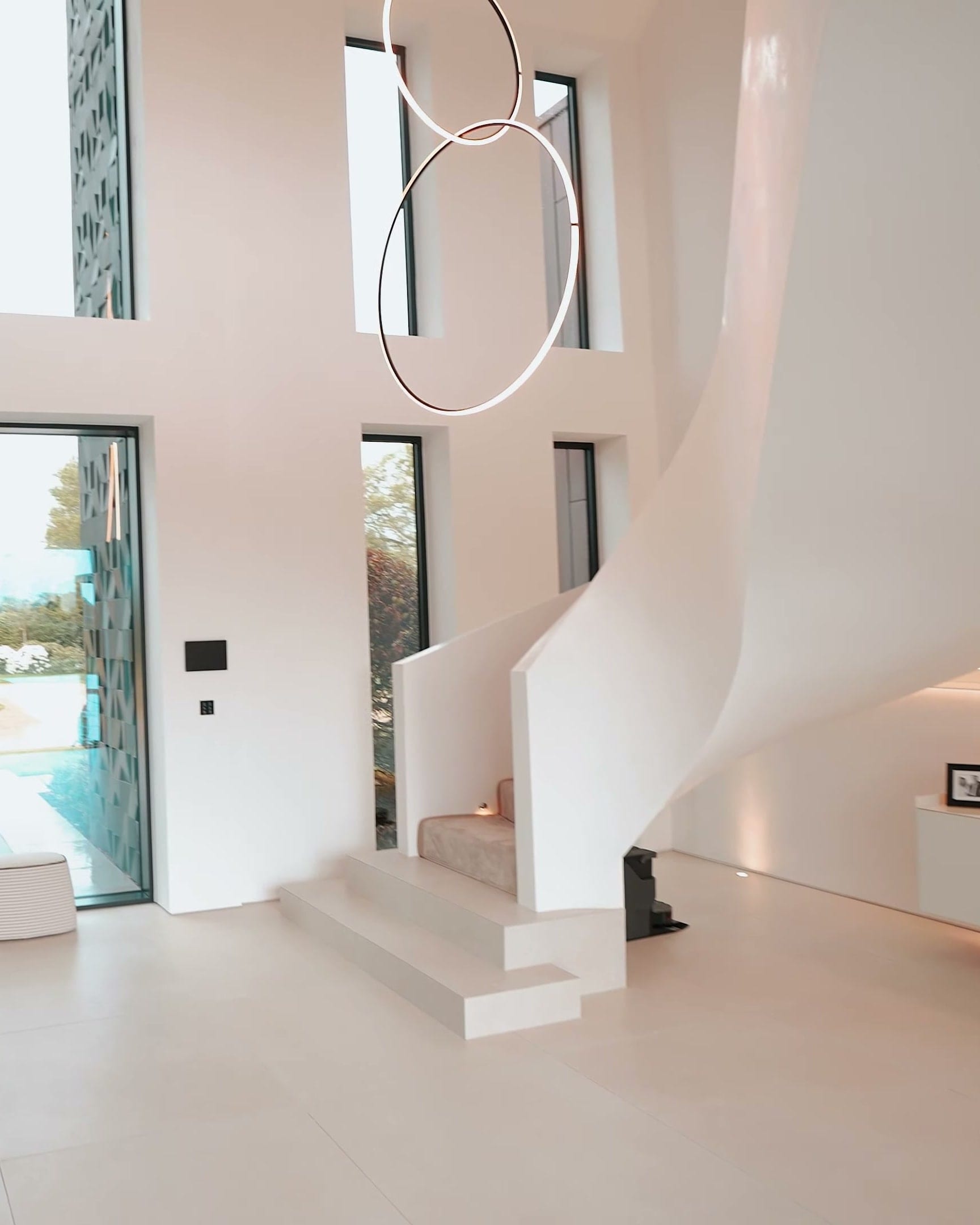 A double height hall with a curving white staircase and ring pendant lights, filmed for applicArt Designs
