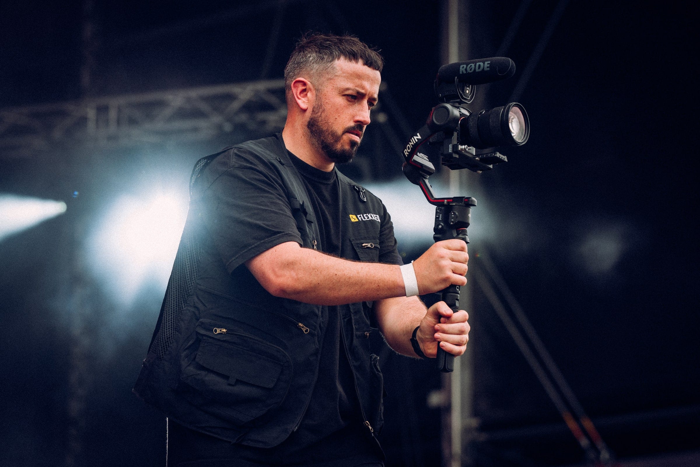 Camera operator with a gimbal against a dark backdrop, stage lights behind