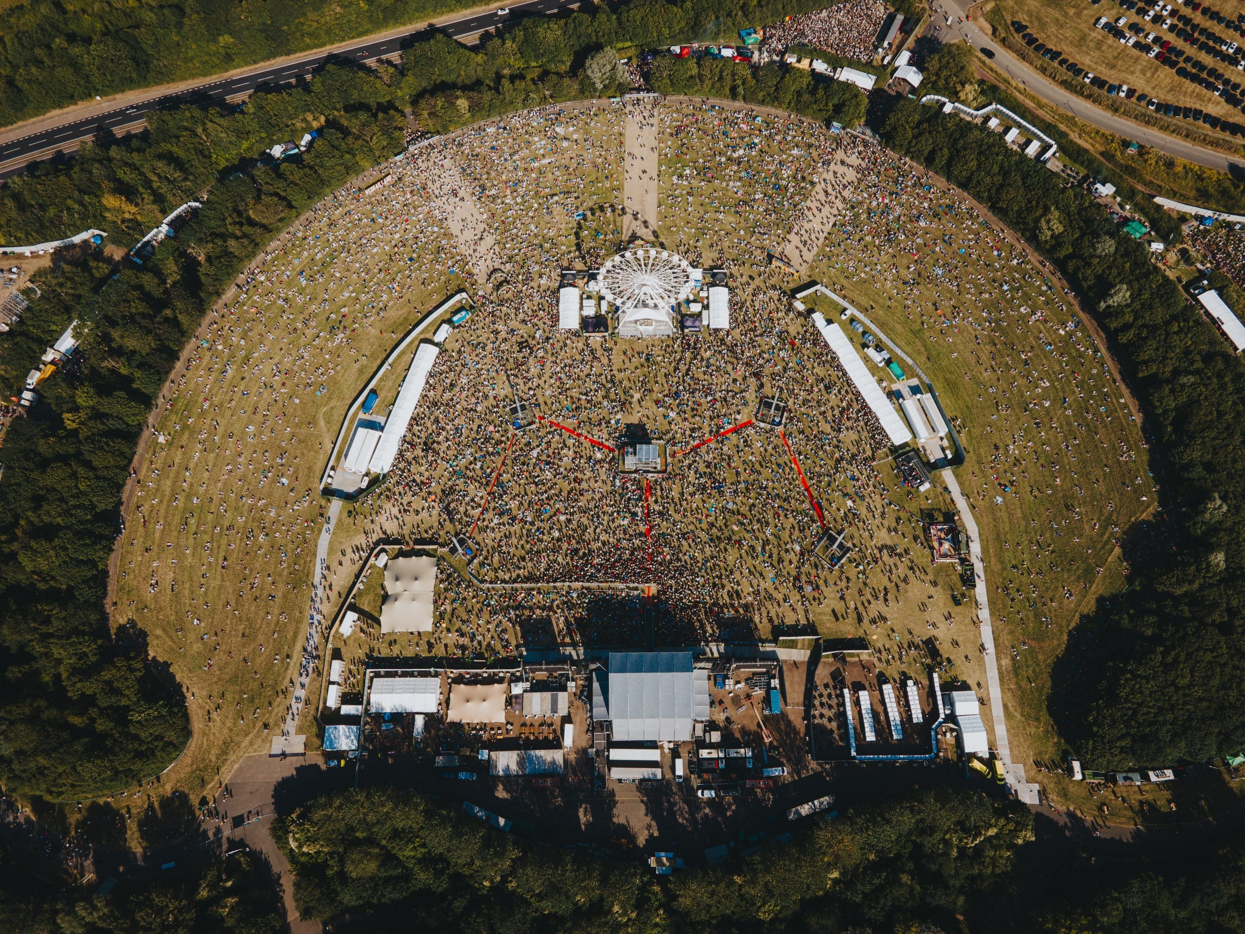 Straight-down aerial of a packed festival bowl, the stage and crowd forming a circle in the landscape