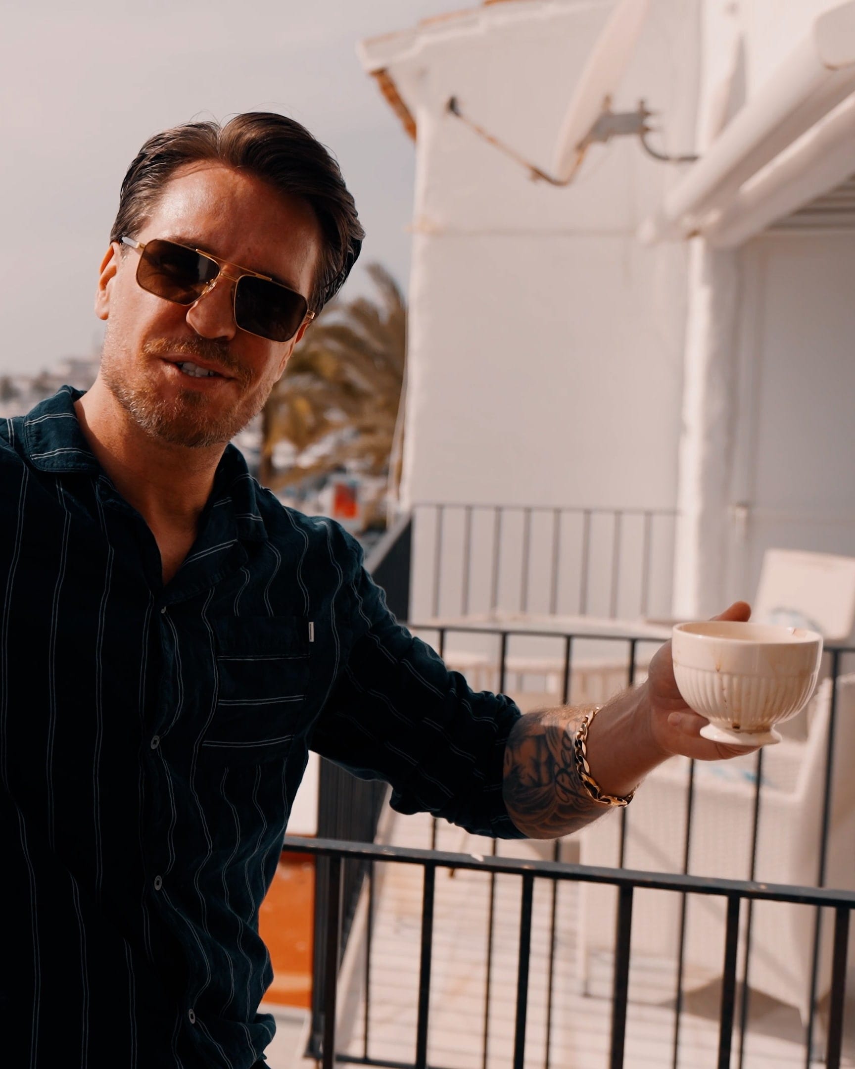 A performer in sunglasses on a balcony above a marina, pointing towards the lens, on a music video shoot