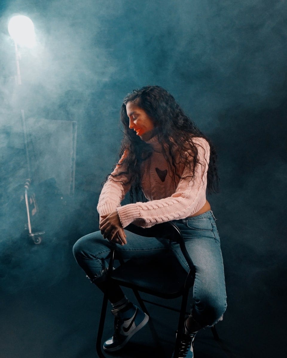 A singer on a stool in blue haze, a camera framing her from the foreground