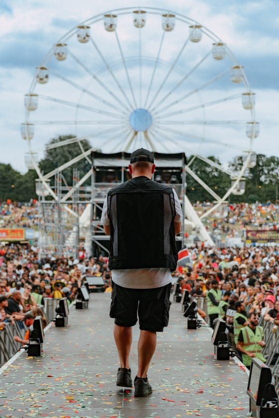 Camera operator walking through a festival crowd with a ferris wheel behind