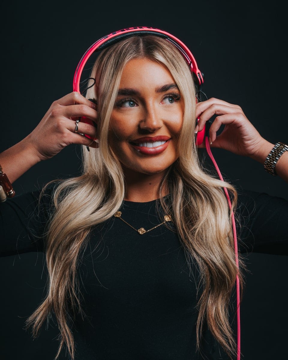 A studio portrait of a woman in pink headphones against a dark backdrop