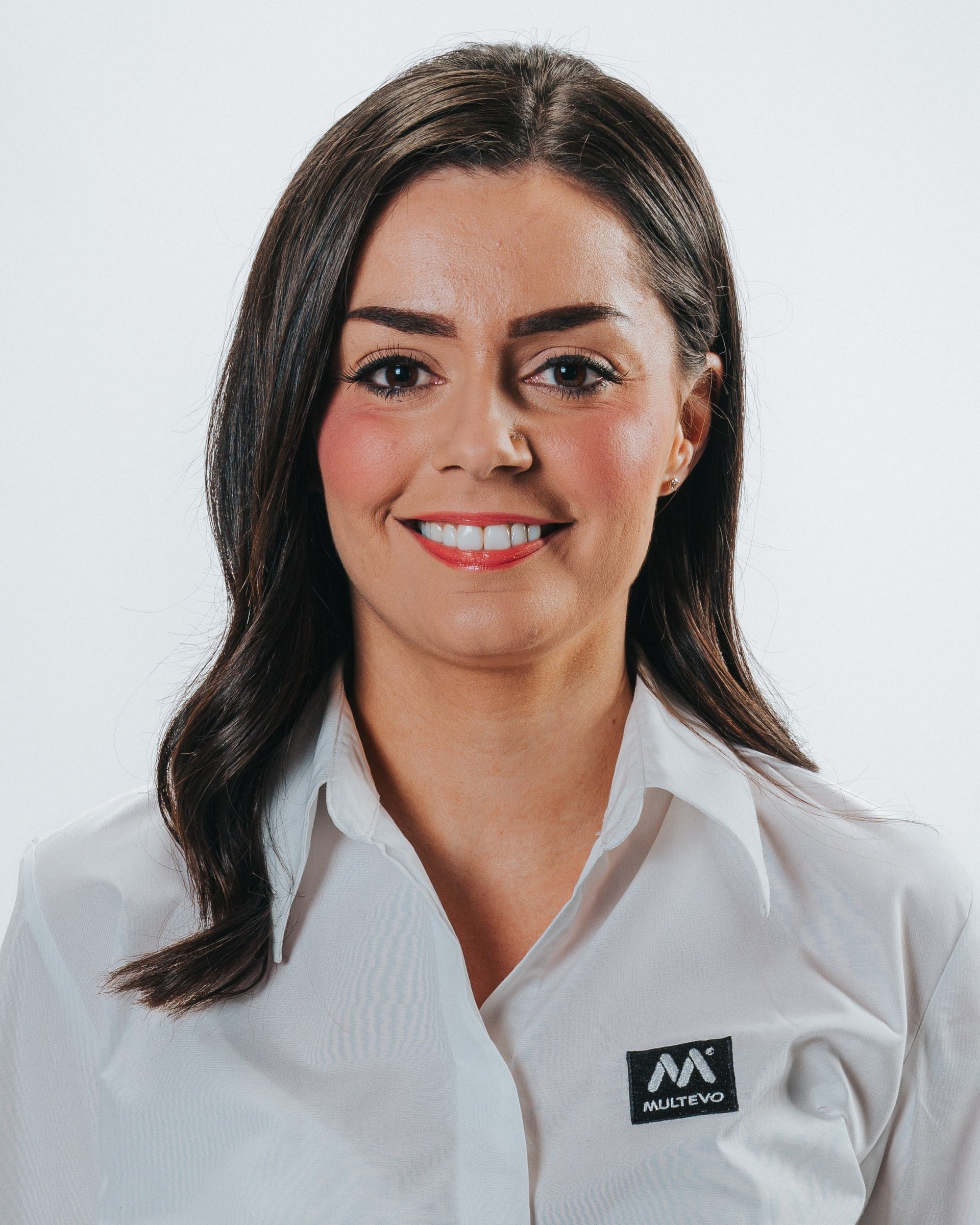 Corporate headshot of a smiling woman with long dark hair in a white branded work shirt, on a pale grey backdrop