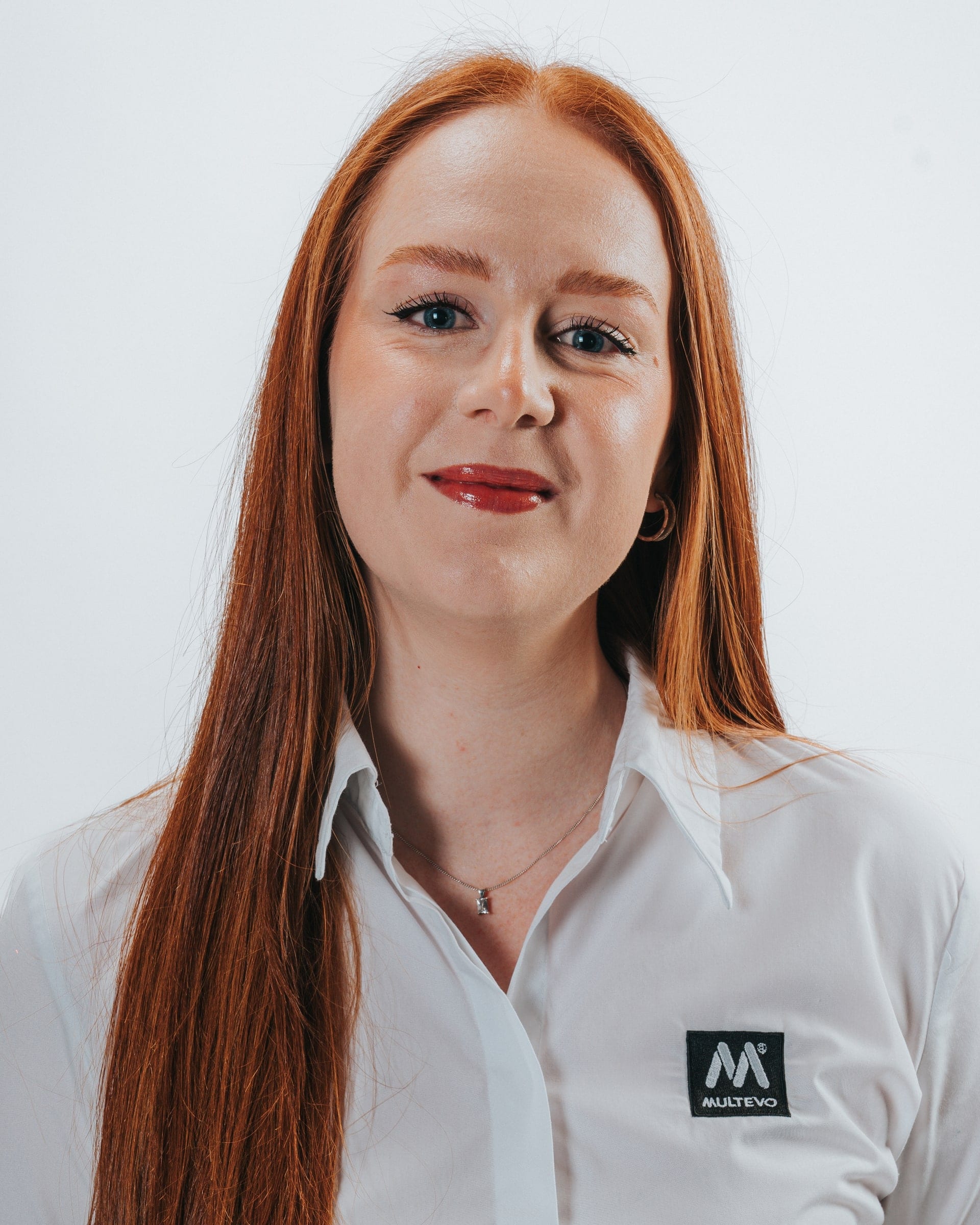 Corporate headshot of a woman with long red hair in a white branded work shirt, on a pale grey backdrop