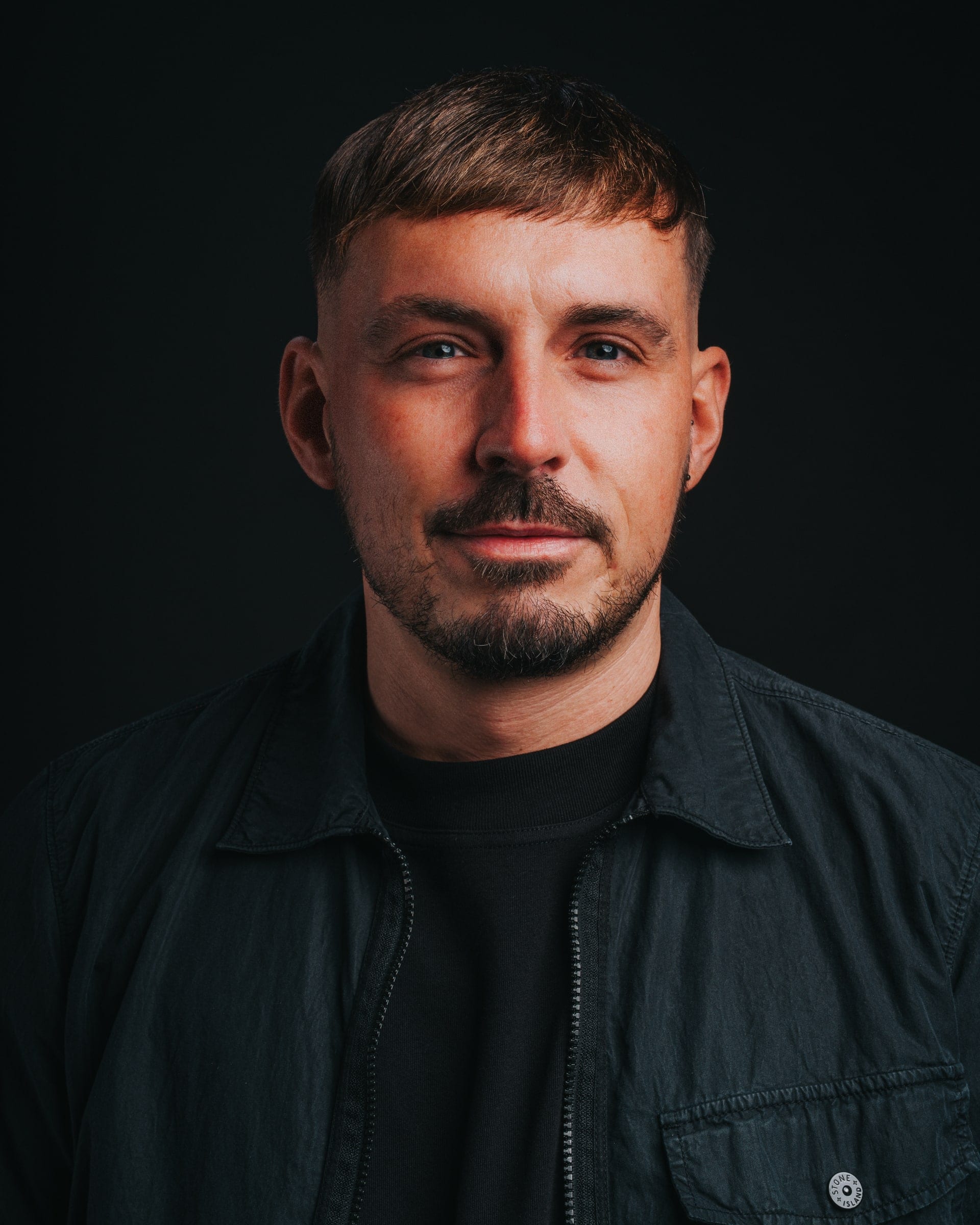 A man in a dark overshirt looking straight to camera