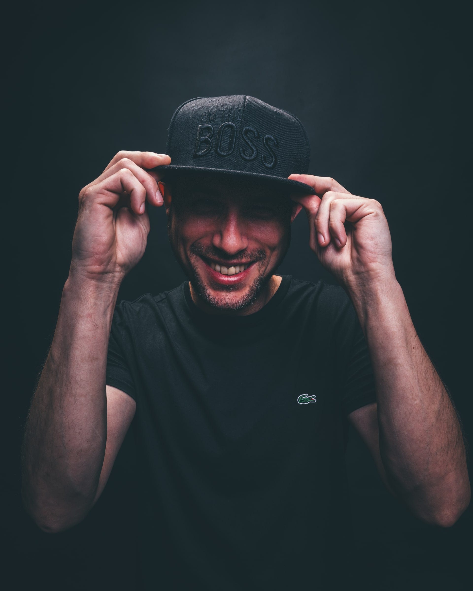 A man grinning under the peak of his cap, both hands on the brim