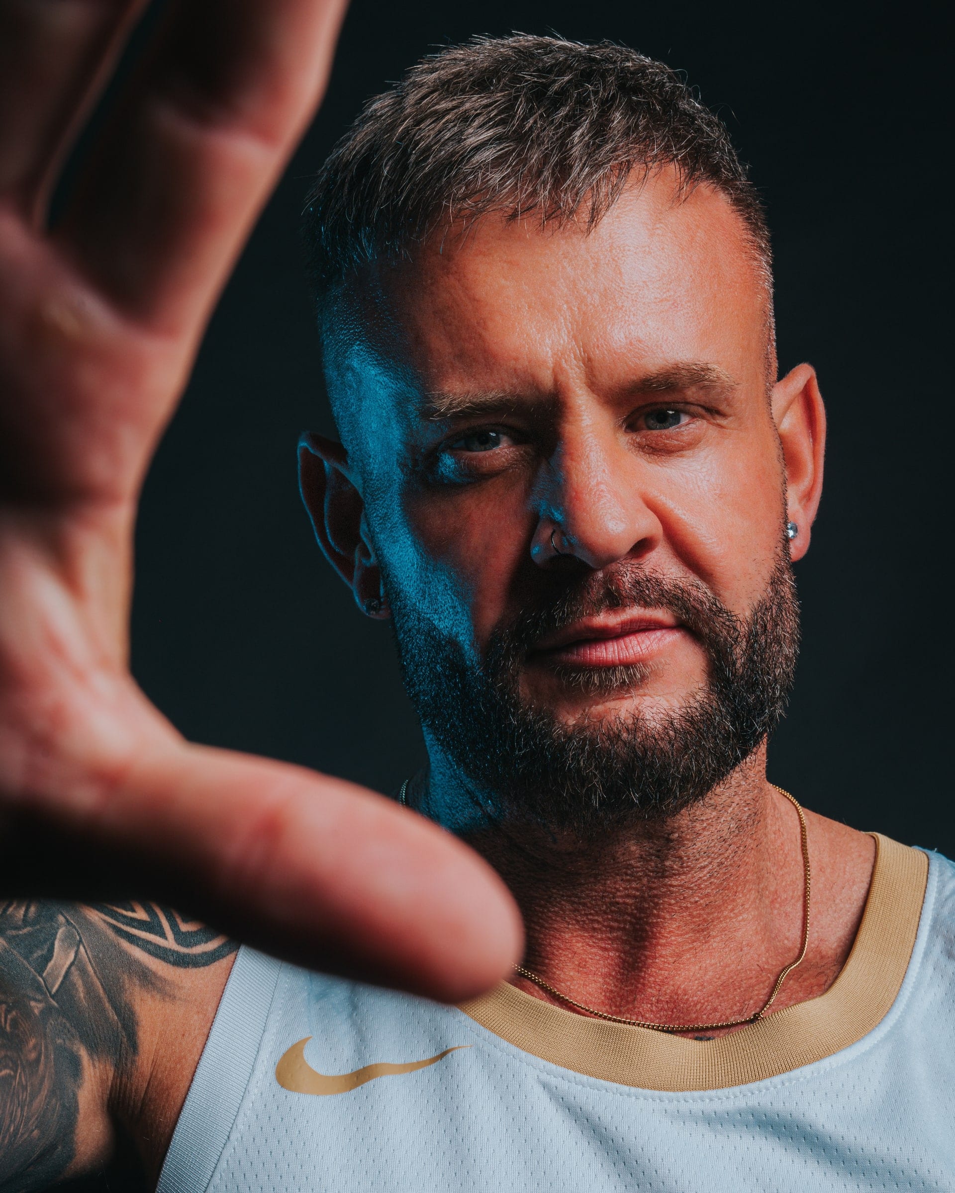 A bearded man in a basketball vest, one hand reaching towards the lens