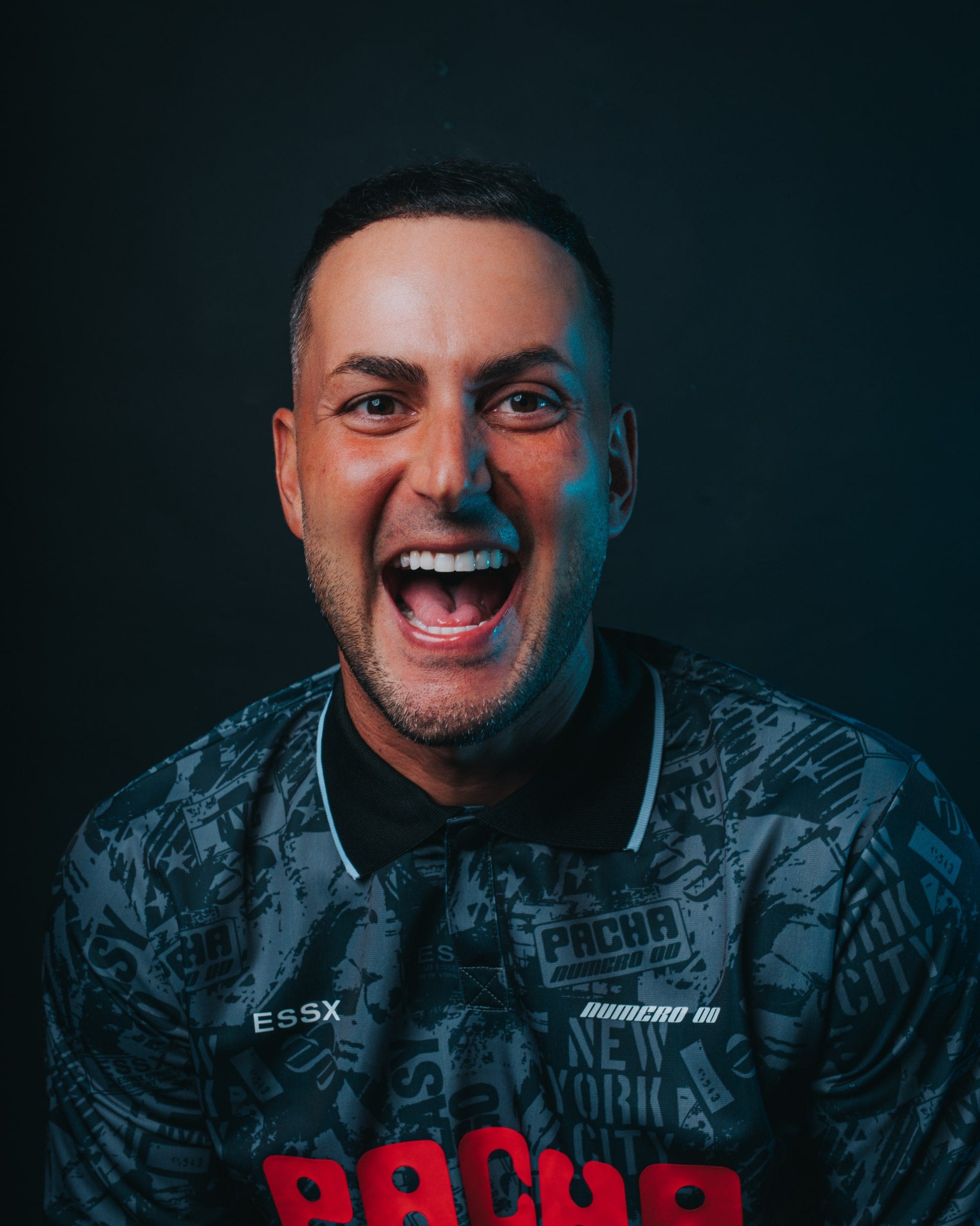 A man laughing to camera in a Pacha football shirt under blue light