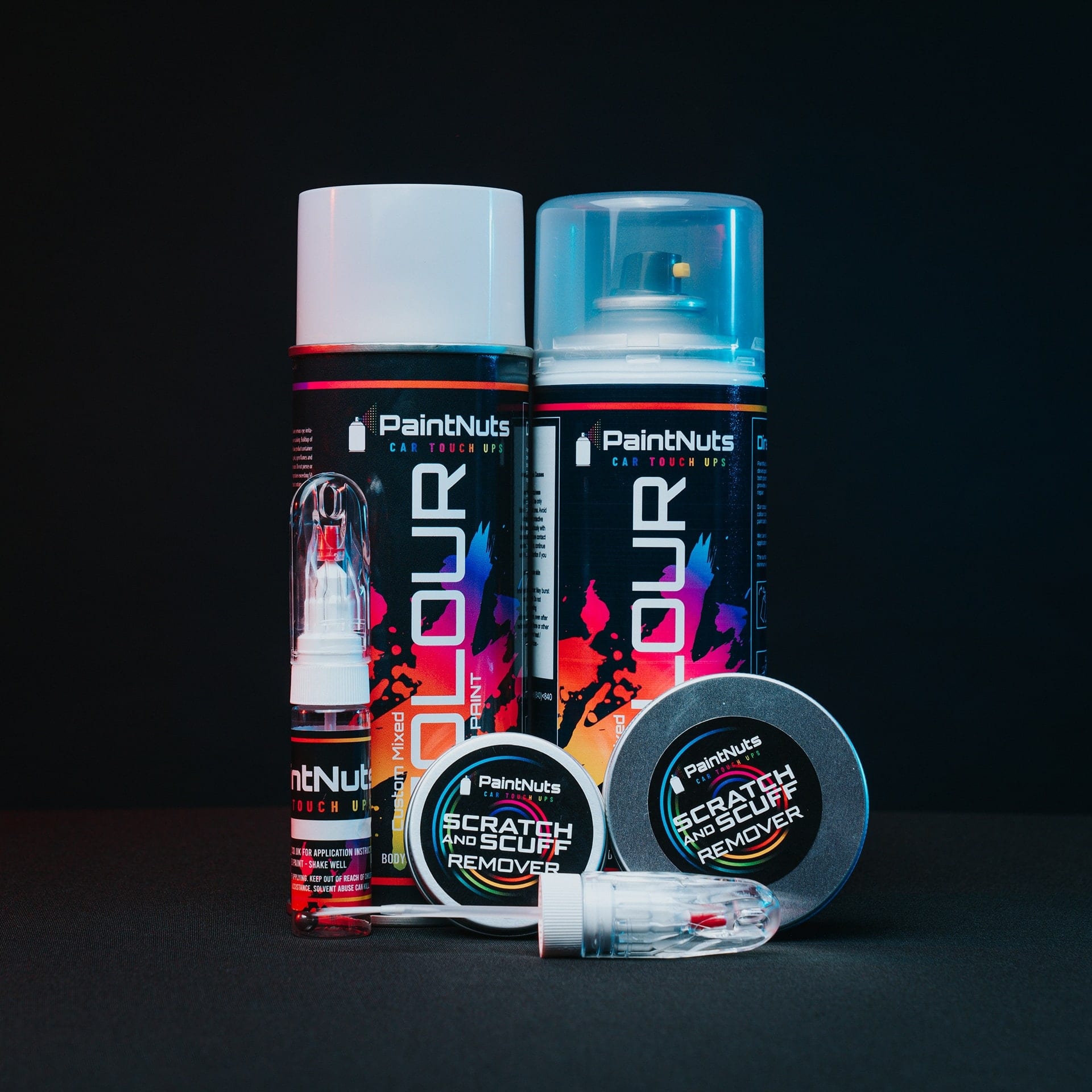 PaintNuts spray cans, touch up pens and scratch remover tins on a black set, lit pink and blue