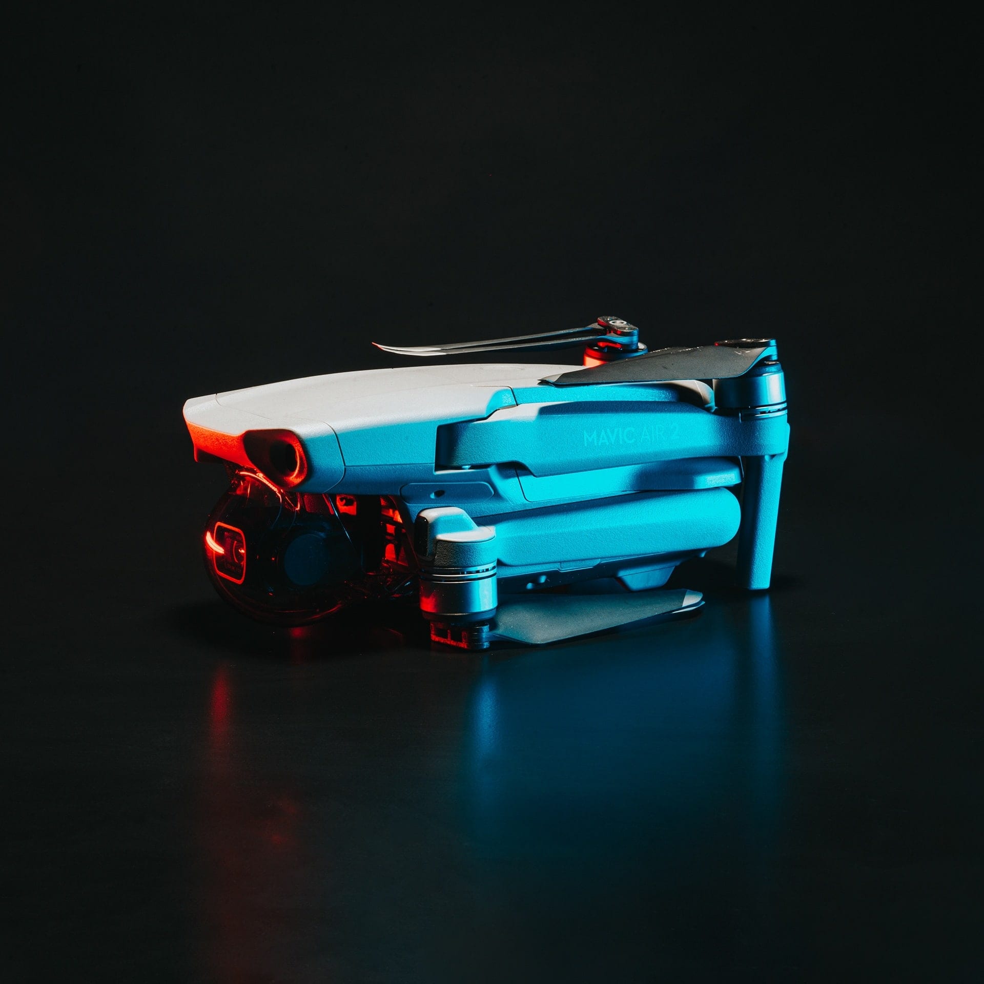 A folded drone on a black surface, rim lit in blue and red