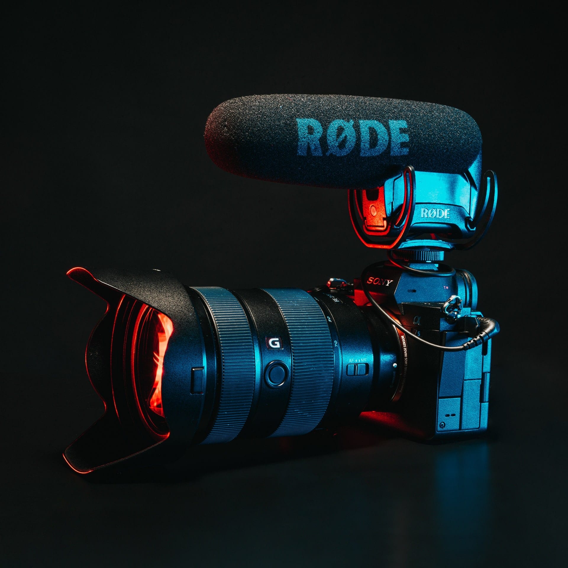 A camera fitted with a RODE microphone, lit red and blue against black