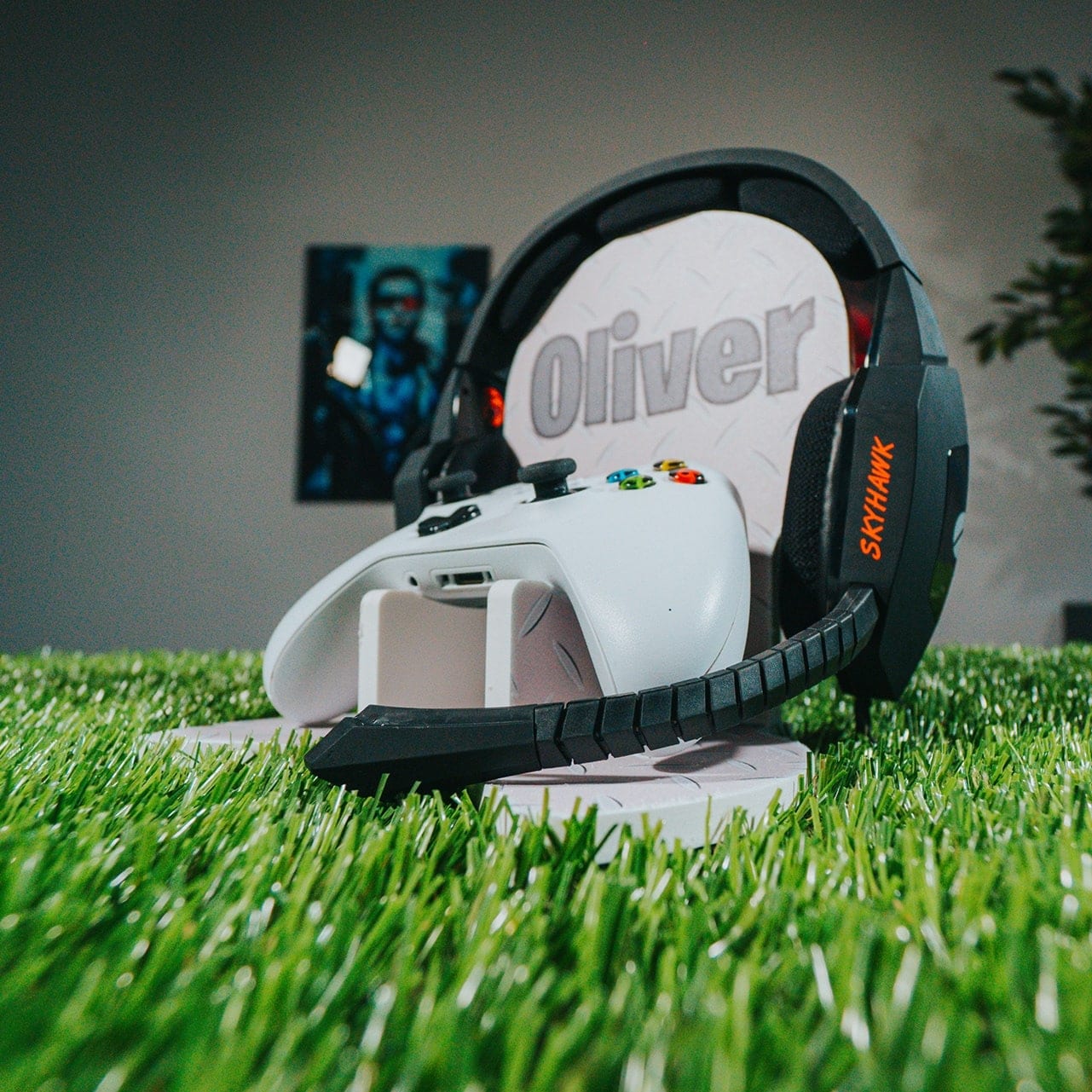 A gaming headset and a white controller on a personalised stand, set on artificial grass