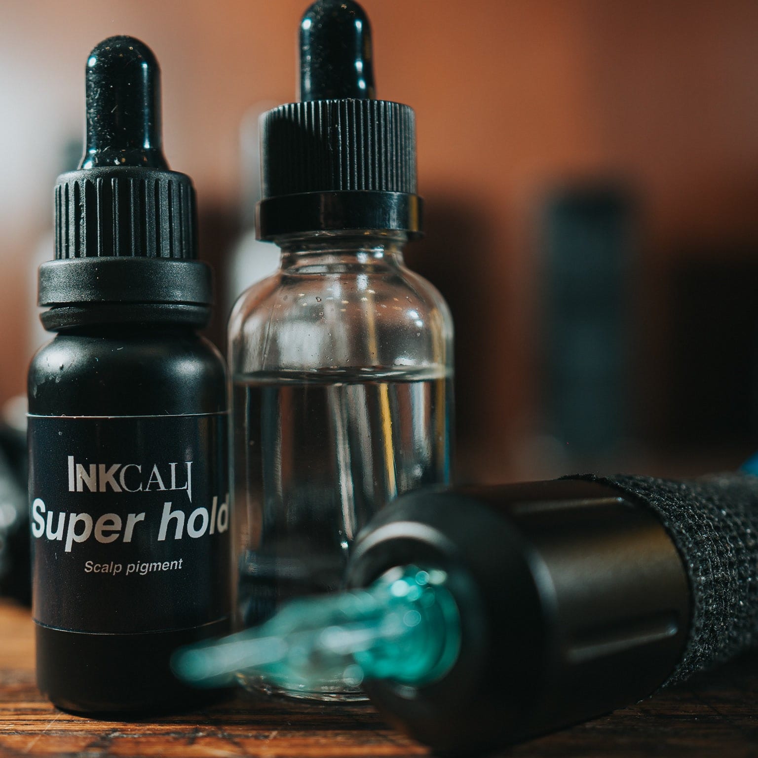 Dropper bottles and a tattoo cartridge on a wooden table, the background warm and soft