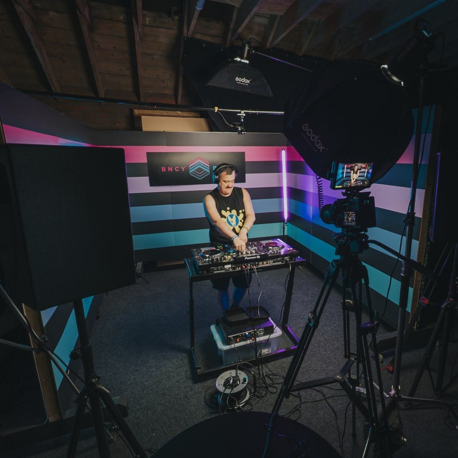 A DJ set being filmed in front of the striped BNCY wall, softboxes and camera monitor in shot