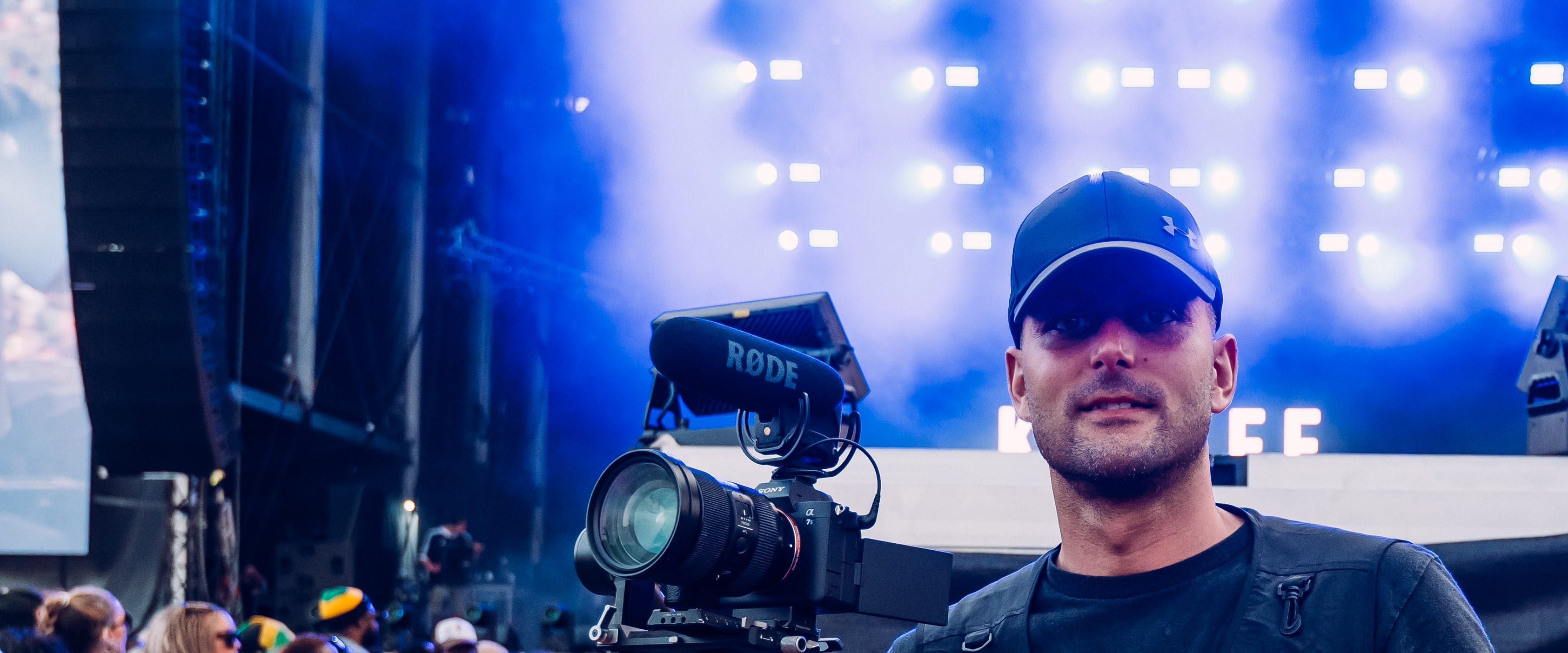 A Flexxed camera operator in a festival pit, a RODE-mounted camera on a gimbal beside him and a lit stage behind
